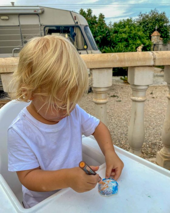 Young boy sat in a highchair outside and painting a plaster shell with an acrylic paint pen