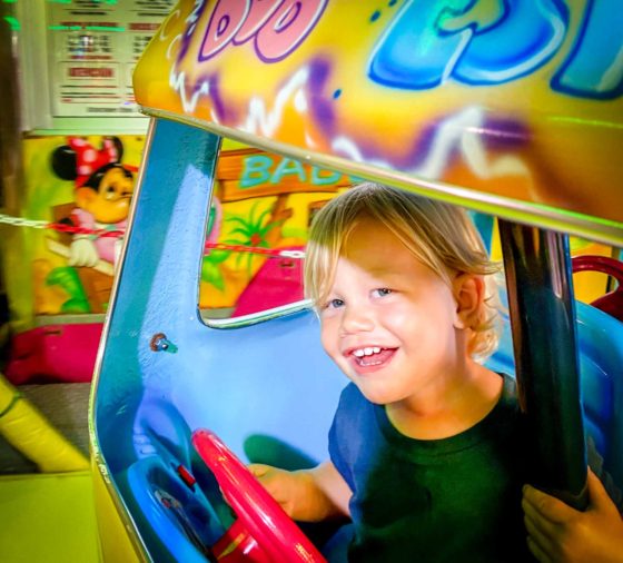 Young boy smiling in a colourful car on a fairground ride