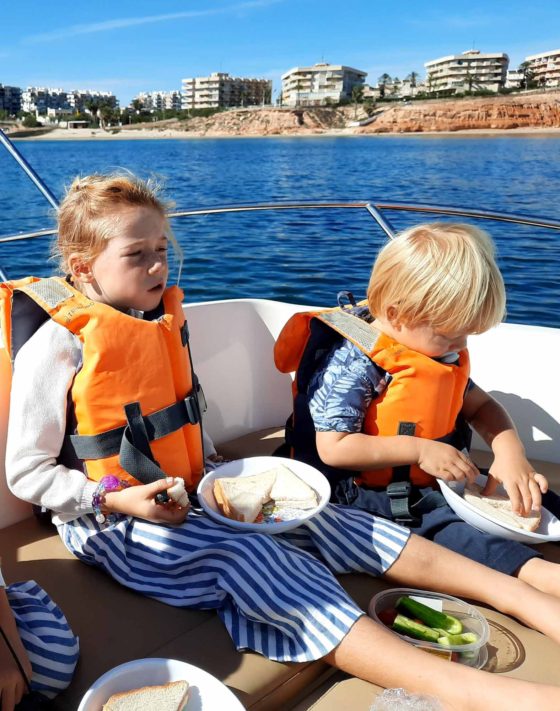 2 young children sat on a boat out at sea, eating sandwiches for a picnic