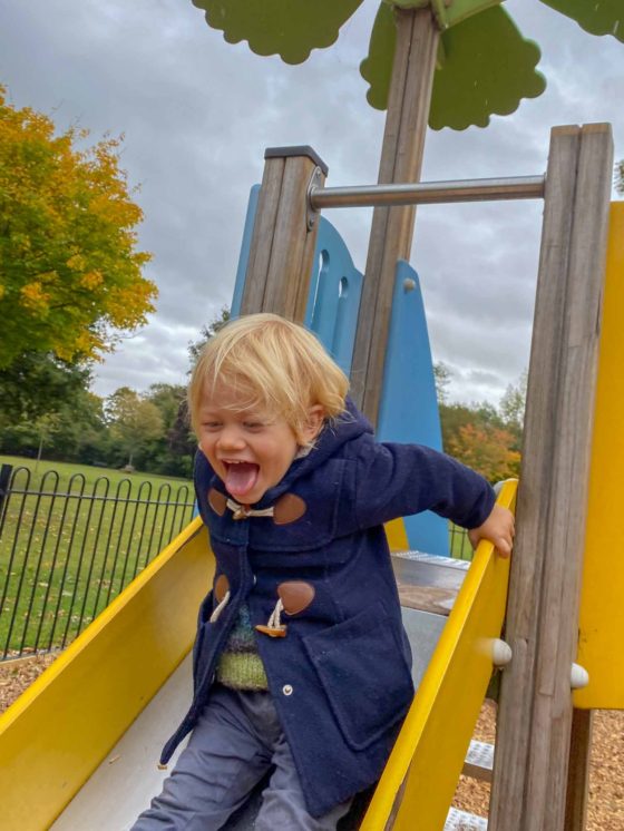 Young boy grinning with his tongue out, going down a slide in a park