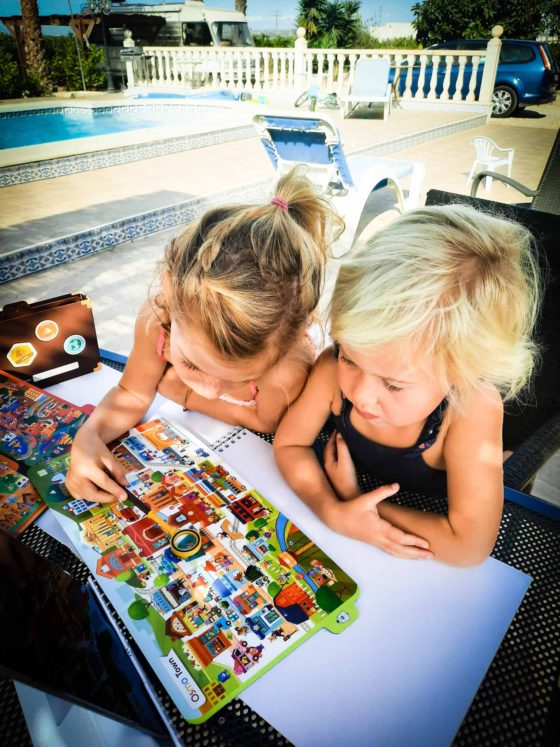 2 young girls with a toy magnifying glass, looking at a colourful cartoon map