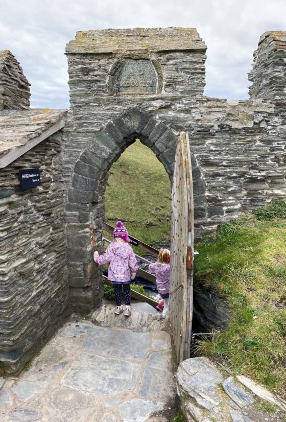 2 small girls in raincoats, descending a staircase through a stone gateway