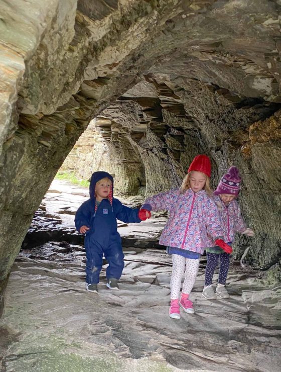 3 young children walking through a rock cave tunnel