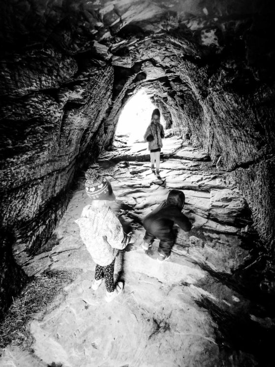 3 small children walking through a stone cave tunnel