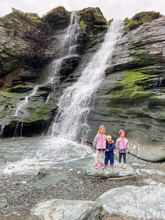 3 small children stood in front of a waterfall on a beach