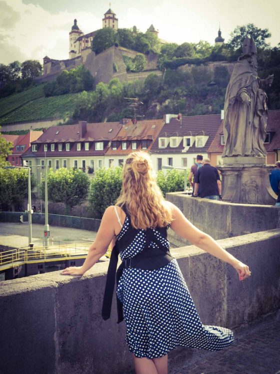 Lady stood on a bridge with stone statue and hilltop palace behind