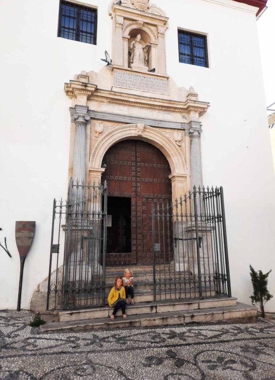 2 young girls sat on a step outside a Spanish church, with mosaic stone floor