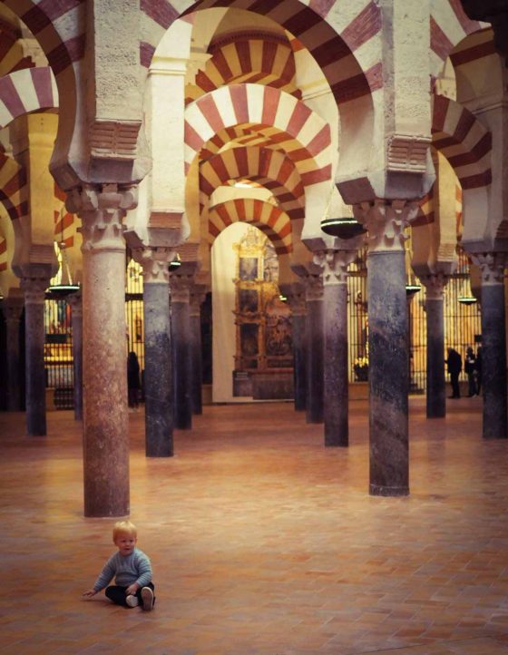 Small boy sat on the floor inside a cathedral, with decorative arches and pillars