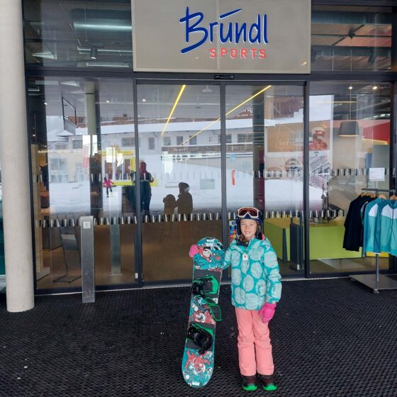 Girl stood holding a snowboard outside of a Brundl Sports shop