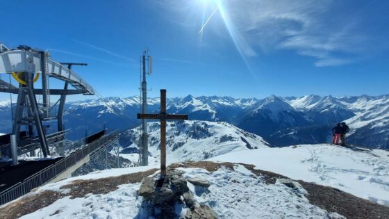 Cross at the top of a snowy mountain, with mountain scenery all around