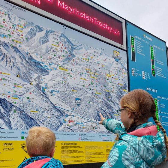 2 children stood in front of a large ski piste map