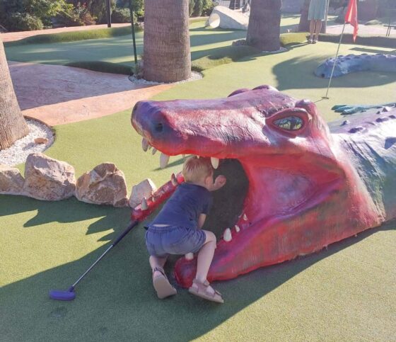 Boy climbing into the mouth of a model crocodile on a mini golf course