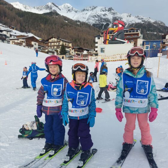 3 children wearing full ski clothing at a ski resort