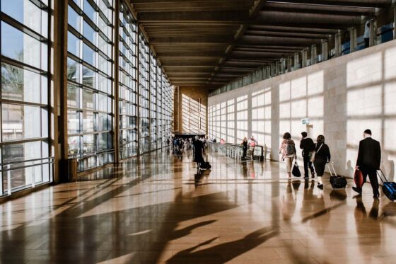 Passengers walking through an airport terminal with floor to ceiling windows on one side