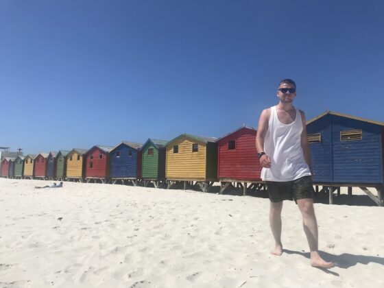 Man walking in front of a line of colourful wooden beach huts