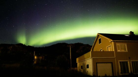Green Aurora Borealis lights in the sky above a brown wooden house