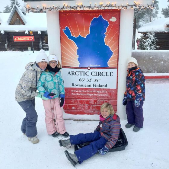 Family in the snow at a sign marking the Arctic Circle line