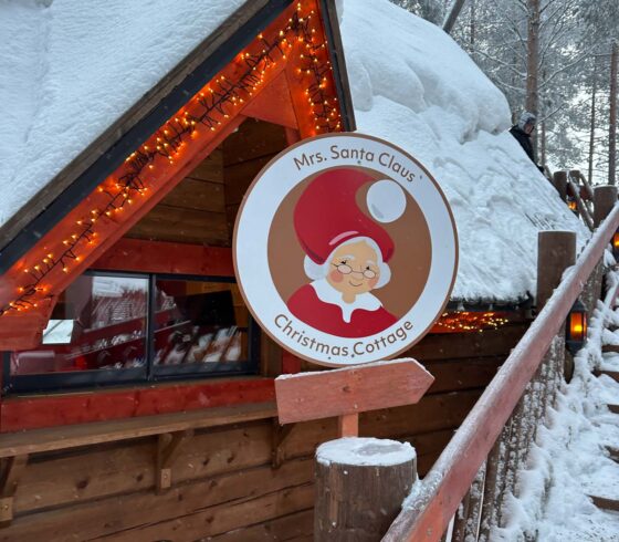 Snow covered wooden cabin, with sign saying 'Mrs Santa Claus' Christmas Cottage'
