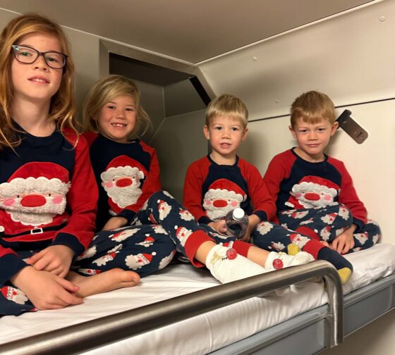 4 small children wearing matching Santa pyjamas sat on a top bunk bed