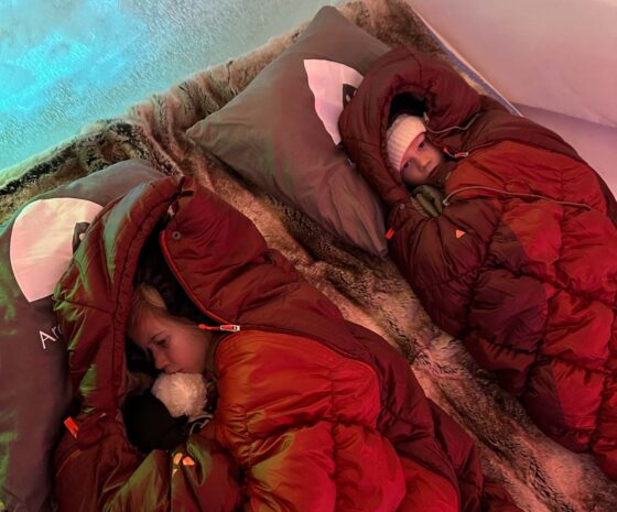 2 children lying in big, puffy sleeping bags in an ice room