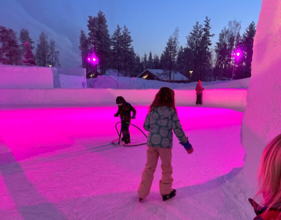 Children ice skating on a small rink illuminated with a pink light