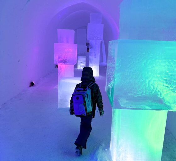 Child wearing winter clothes and a backpack walking into an illuminated snow tunnel