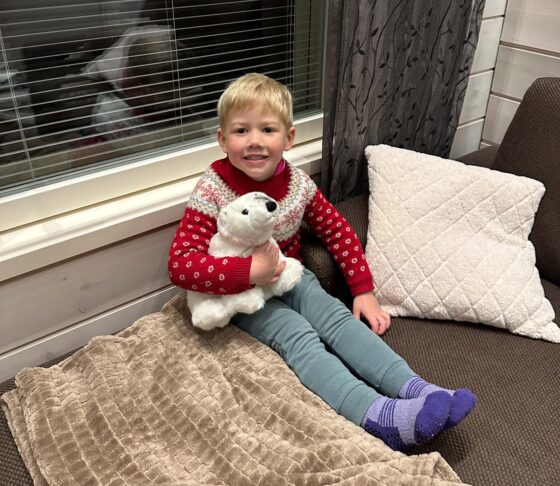 Small boy wearing a red patterned jumper cuddling a toy polar bear