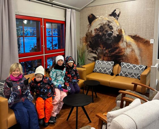 4 children wearing winter clothes sat on a sofa with a picture of a bear on the wall