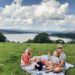 Family with small children eating a picnic on a rug, with lake views behind